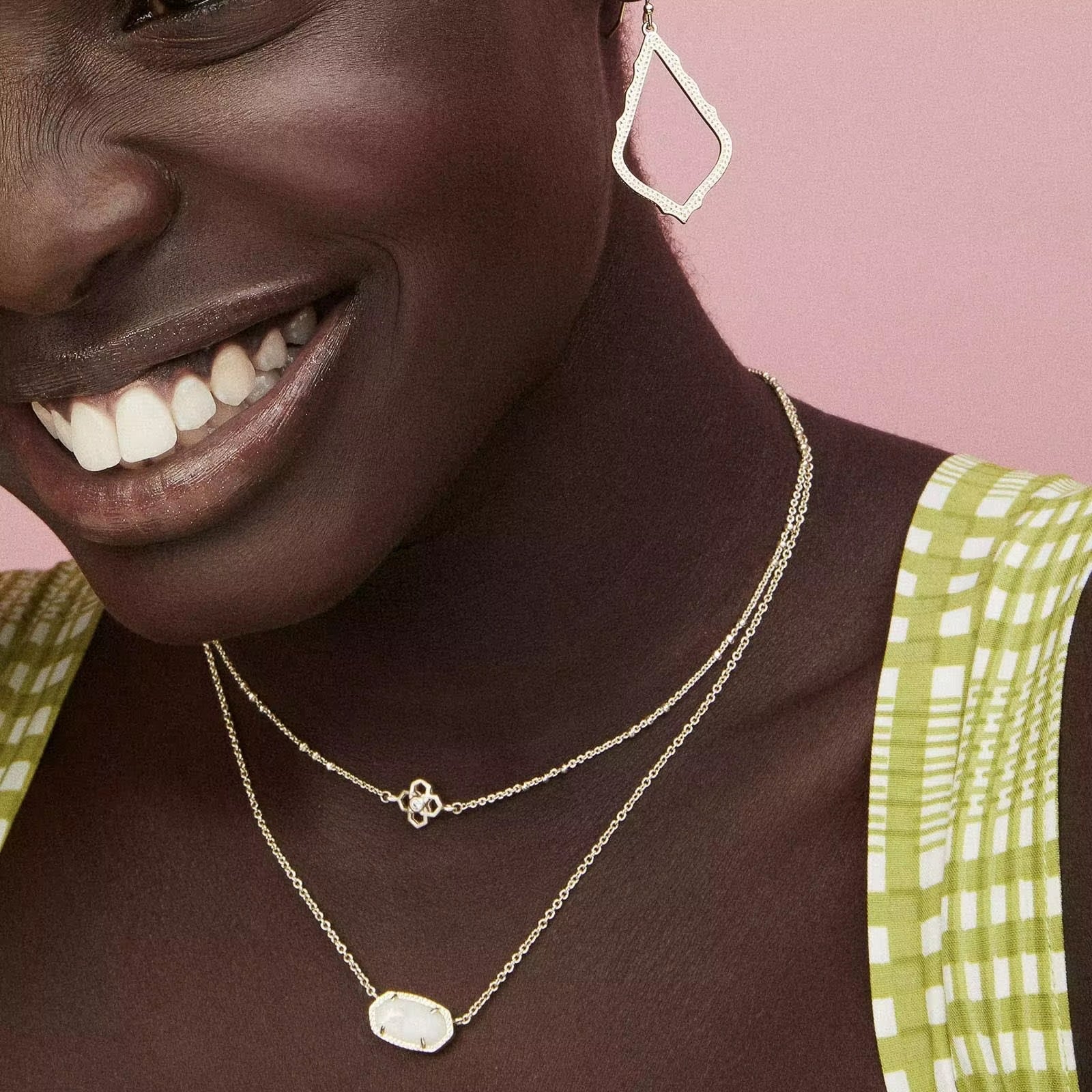 Woman wearing gold necklaces and earrings against a pink background