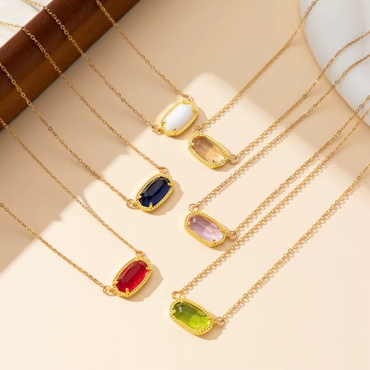 Gold necklaces with colorful gemstones on a beige surface