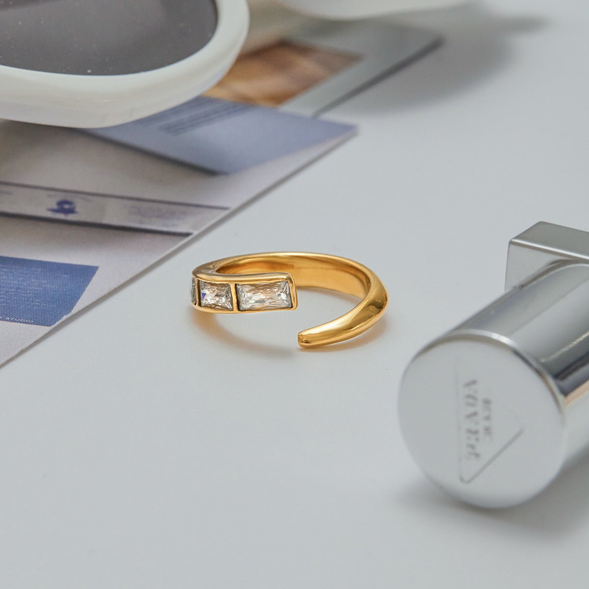 Gold ring with diamonds on a white surface next to a Prada container