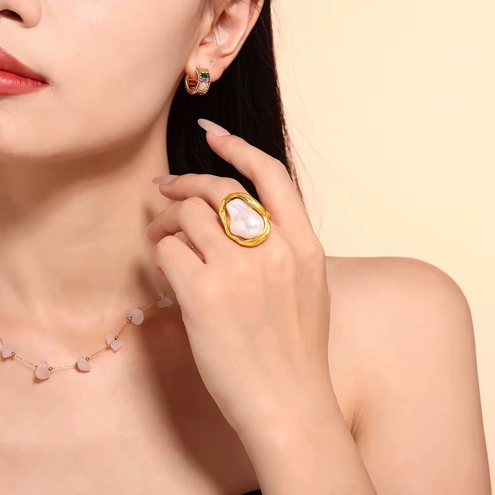 Close-up of a woman wearing gold earrings and a gold ring with a large gemstone on a beige background