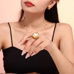 Woman wearing a gold ring with a heart-shaped gemstone on a beige background