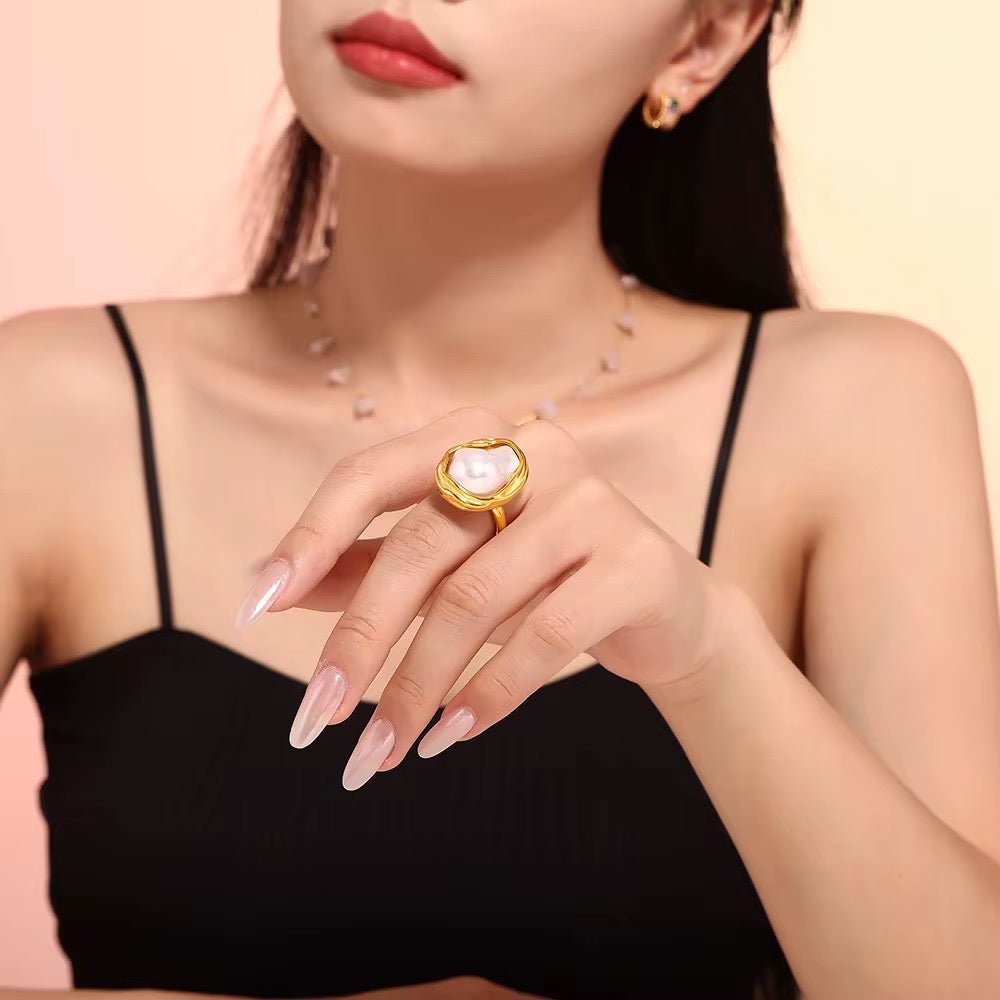 Woman wearing a gold ring with a heart-shaped gemstone on a beige background