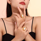 Close-up of a woman's hand wearing gold rings with pearl-like stones on a neutral background