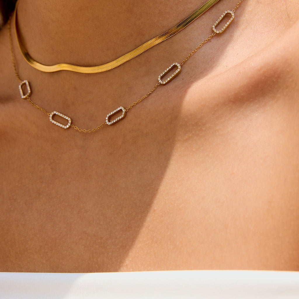 Gold necklace with geometric pendants on a person's neck against a neutral background