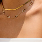 Gold necklace with geometric pendants on a person's neck against a neutral background