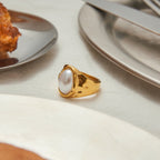 Gold ring with a pearl on a table setting with plates and cutlery.