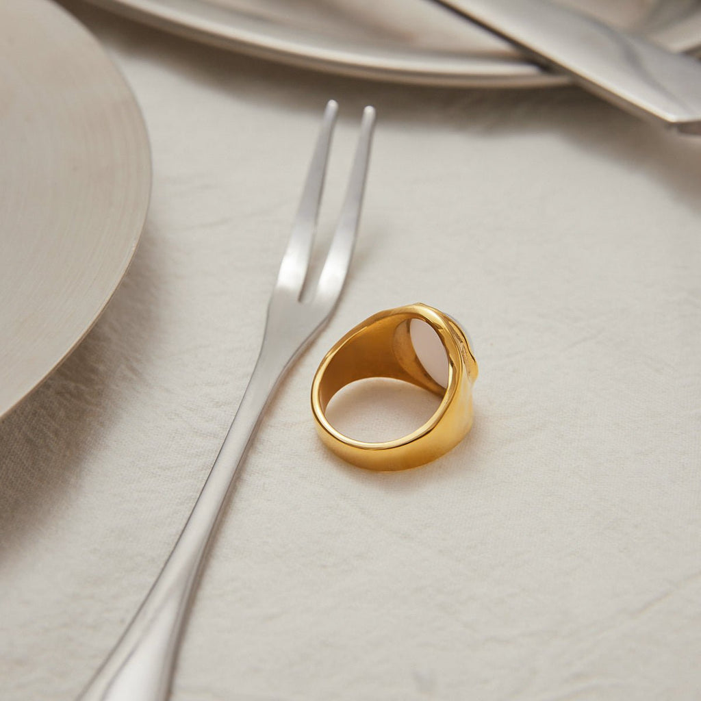 Gold ring on a white surface with a fork and knife in the background