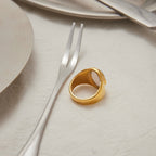 Gold ring on a white surface with a fork and knife in the background
