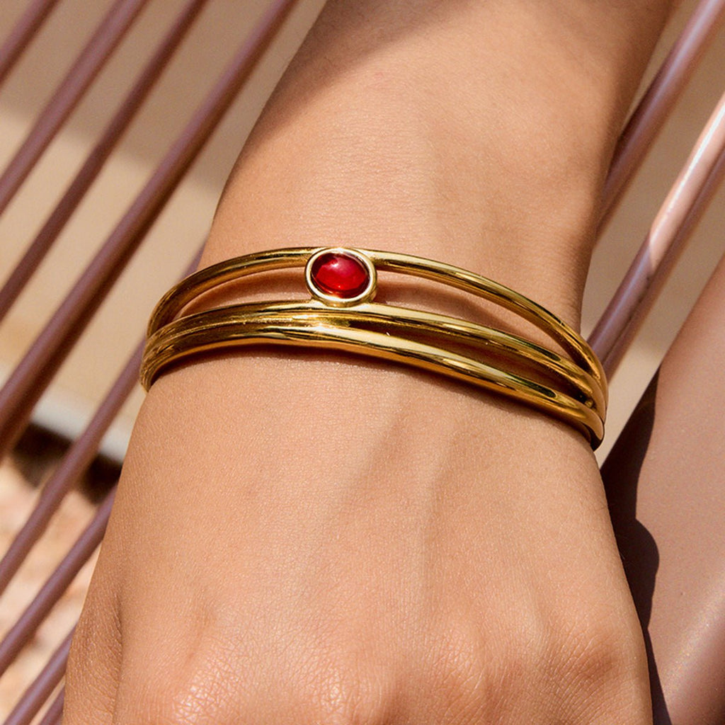Gold cuff bracelet with red garnet on neutral background