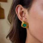 Gold earrings with green gemstones worn by a person