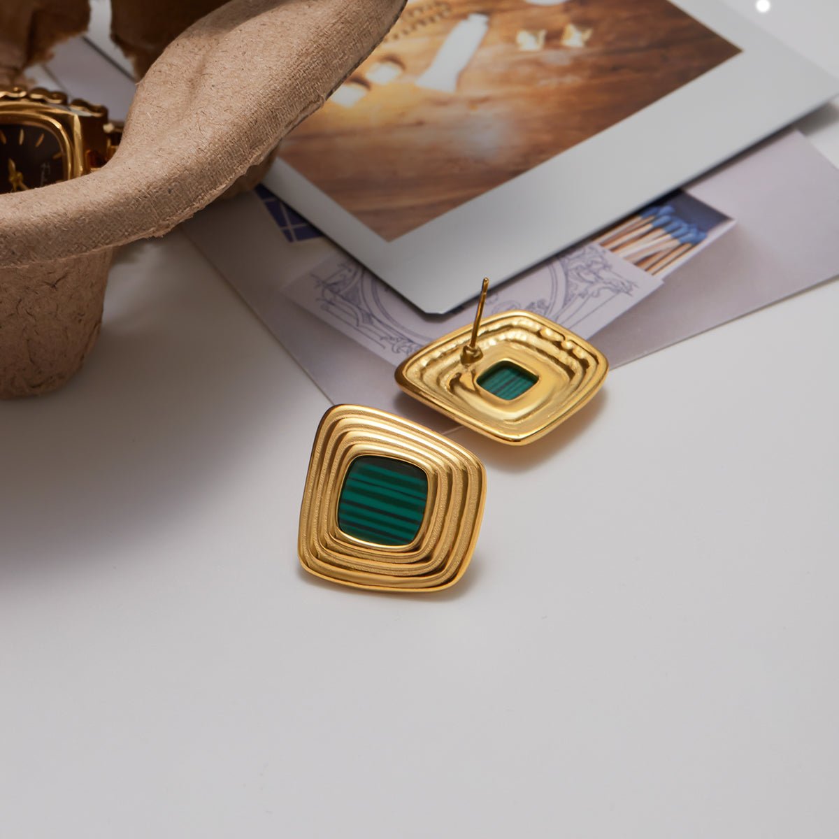 Gold earrings with green stones on a white surface