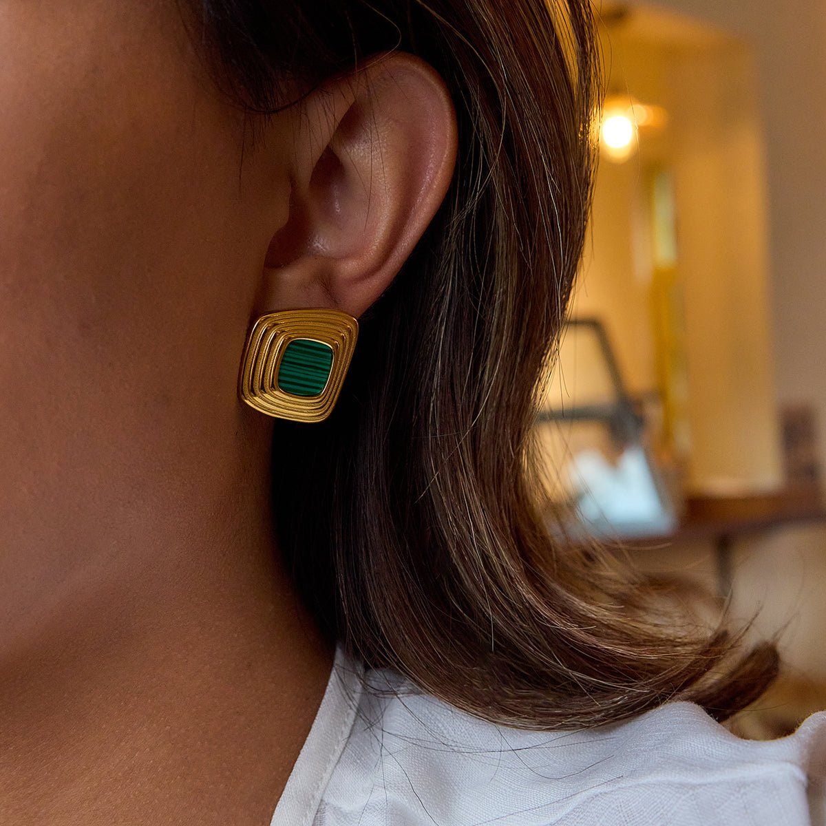 Close-up of a person wearing gold earrings with green stones.
