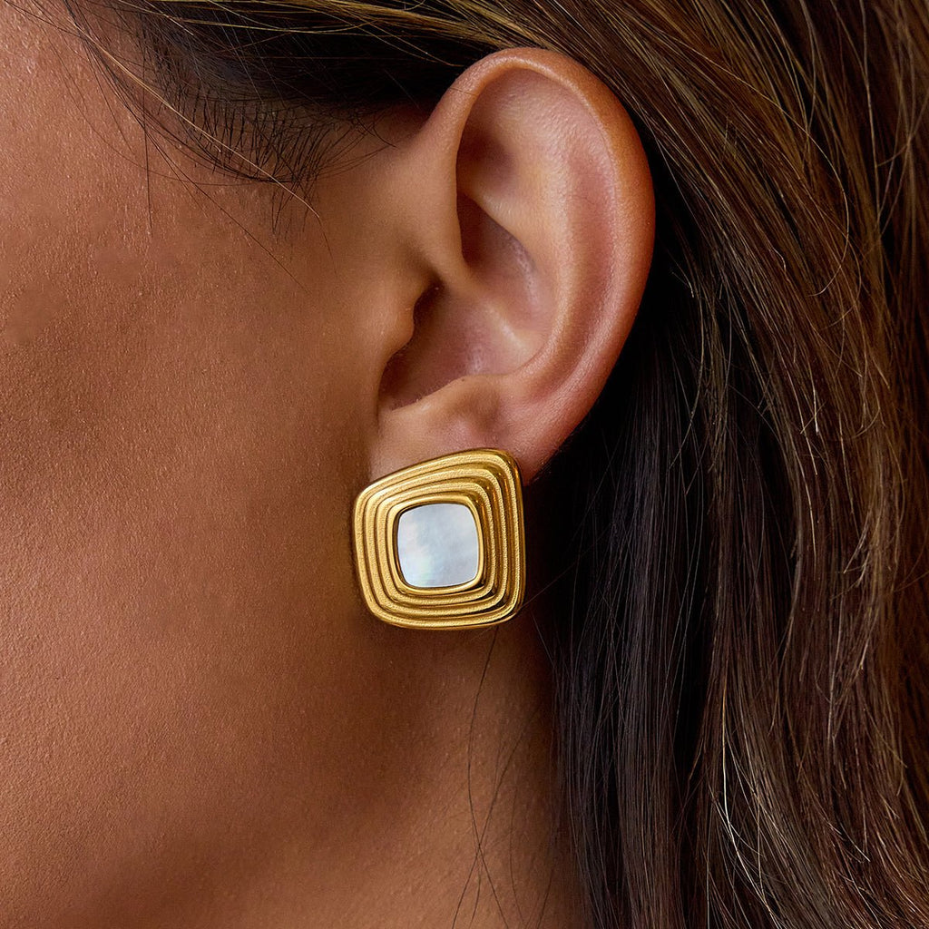 Gold earring with a central gemstone worn by a person Square ripple gold earrings with white center

