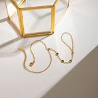 Gold necklace with green gemstones on a white surface with a gold box in the background