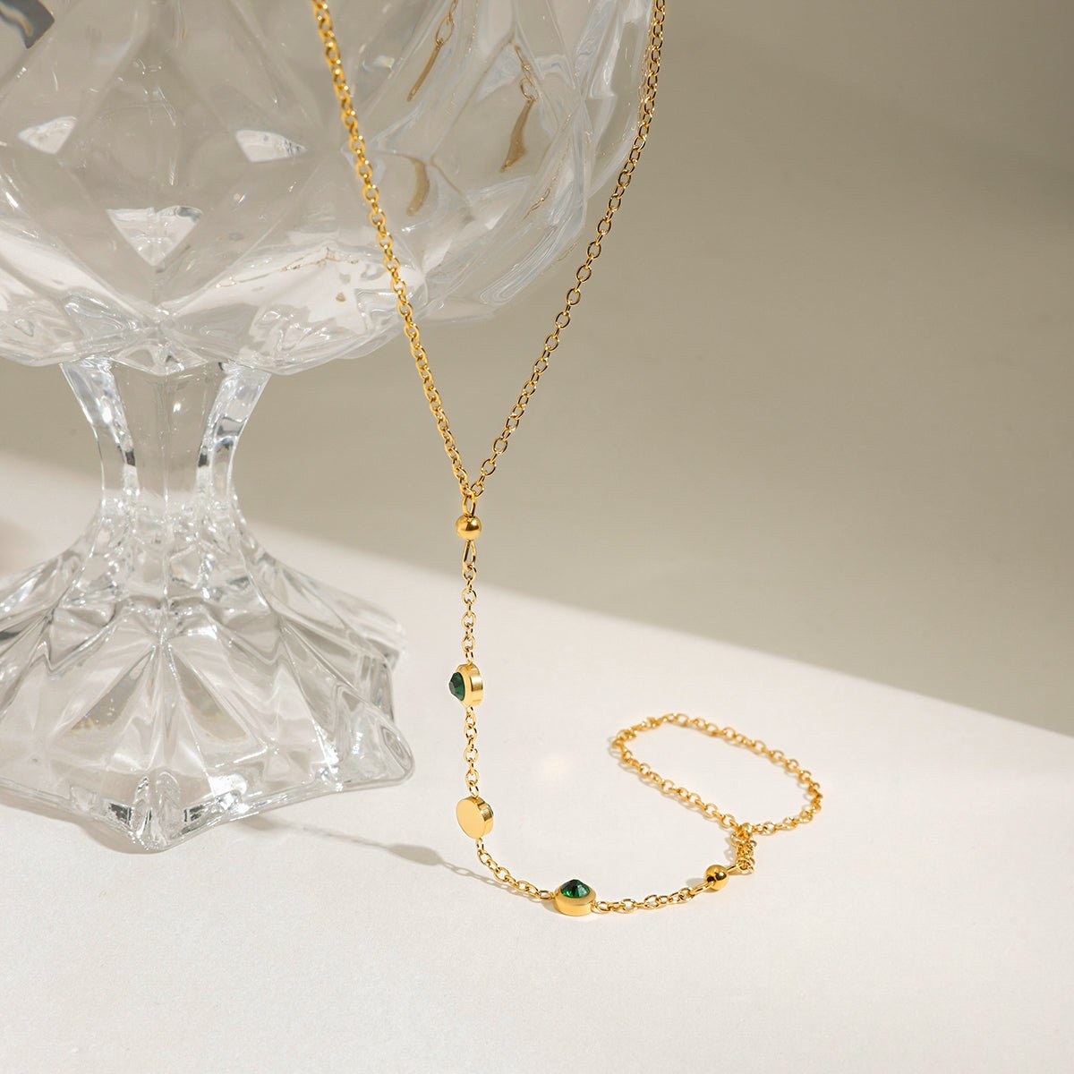 Gold necklace with green beads on a white surface with a glass pedestal