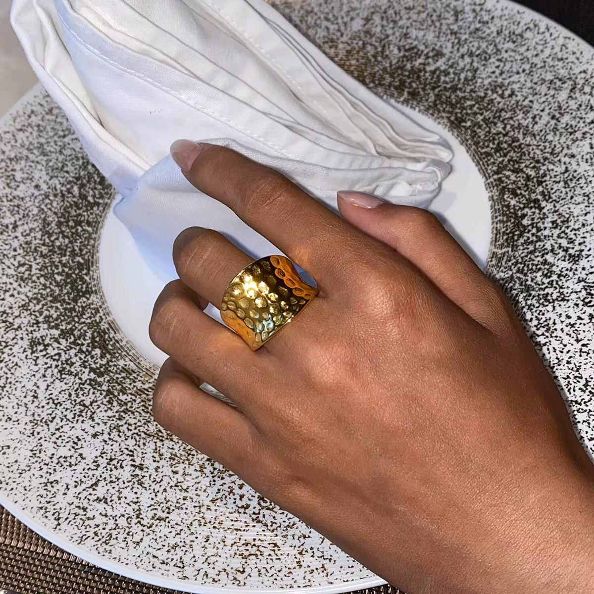 Hand wearing a gold ring on a textured surface with white napkins.