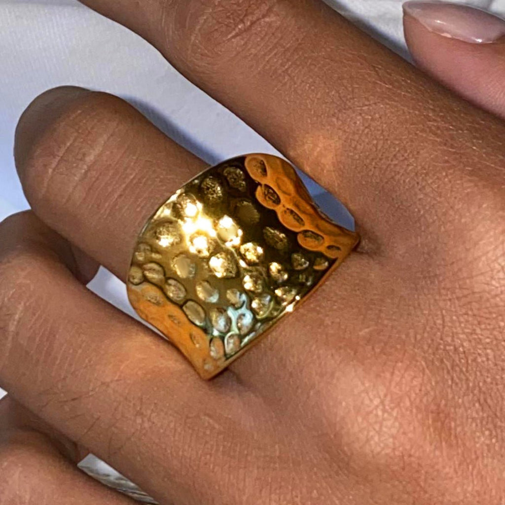 Gold textured ring on a finger against a white background