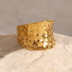 Gold textured ring on a light stone surface with a neutral background