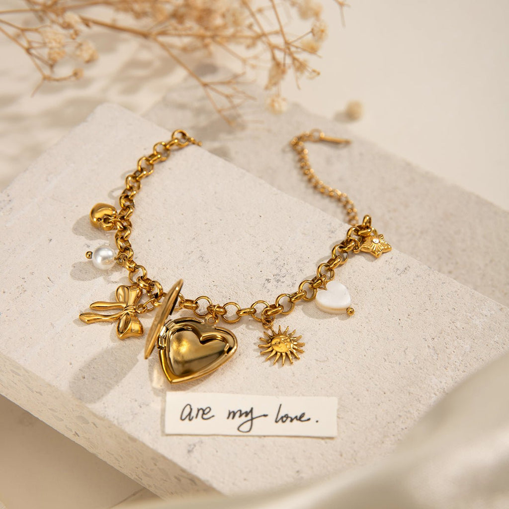 Gold bracelet with heart charm on a textured surface with dried flowers.