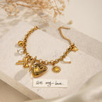 Gold bracelet with heart charm on a textured surface with dried flowers.