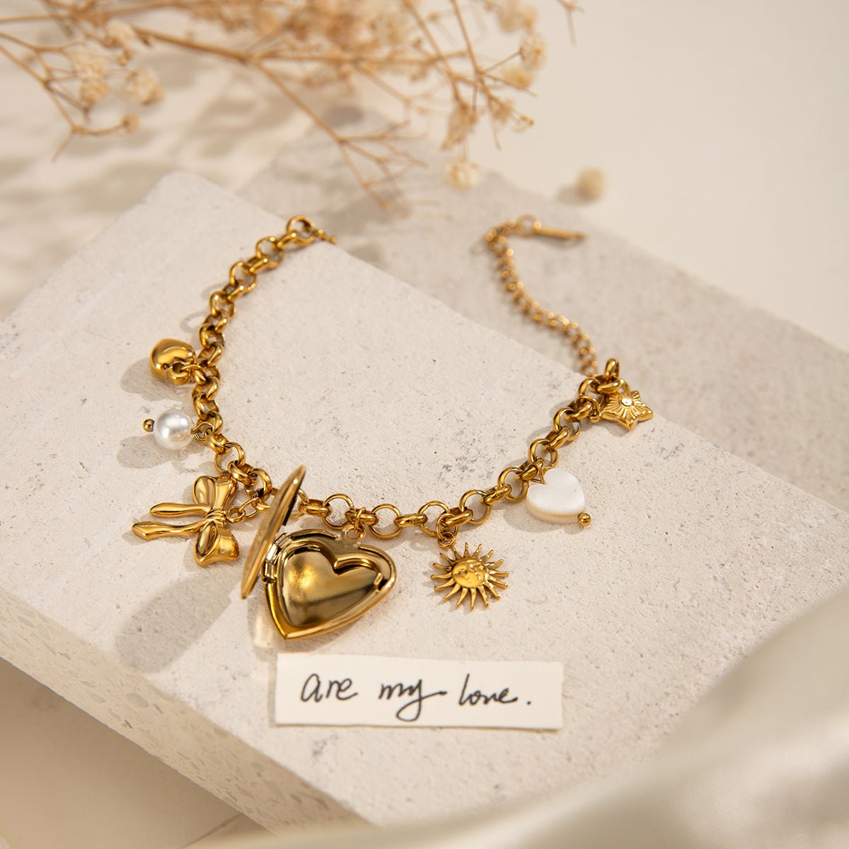 Gold bracelet with heart charm on a textured surface with dried flowers.