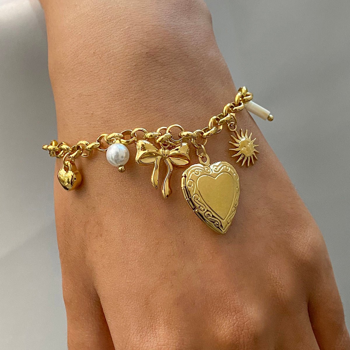 Locket Gold charm bracelet on a wrist with various charms against a neutral background