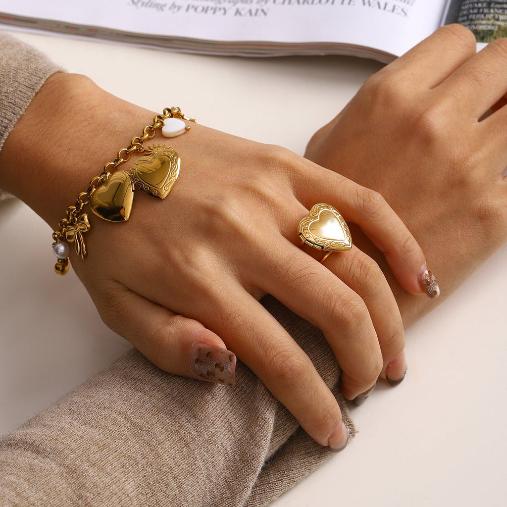 Close-up of a hand wearing a gold heart-shaped ring and bracelet on a neutral background