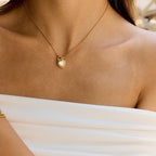 Gold necklace with a heart-shaped pendant on a person wearing a white top.