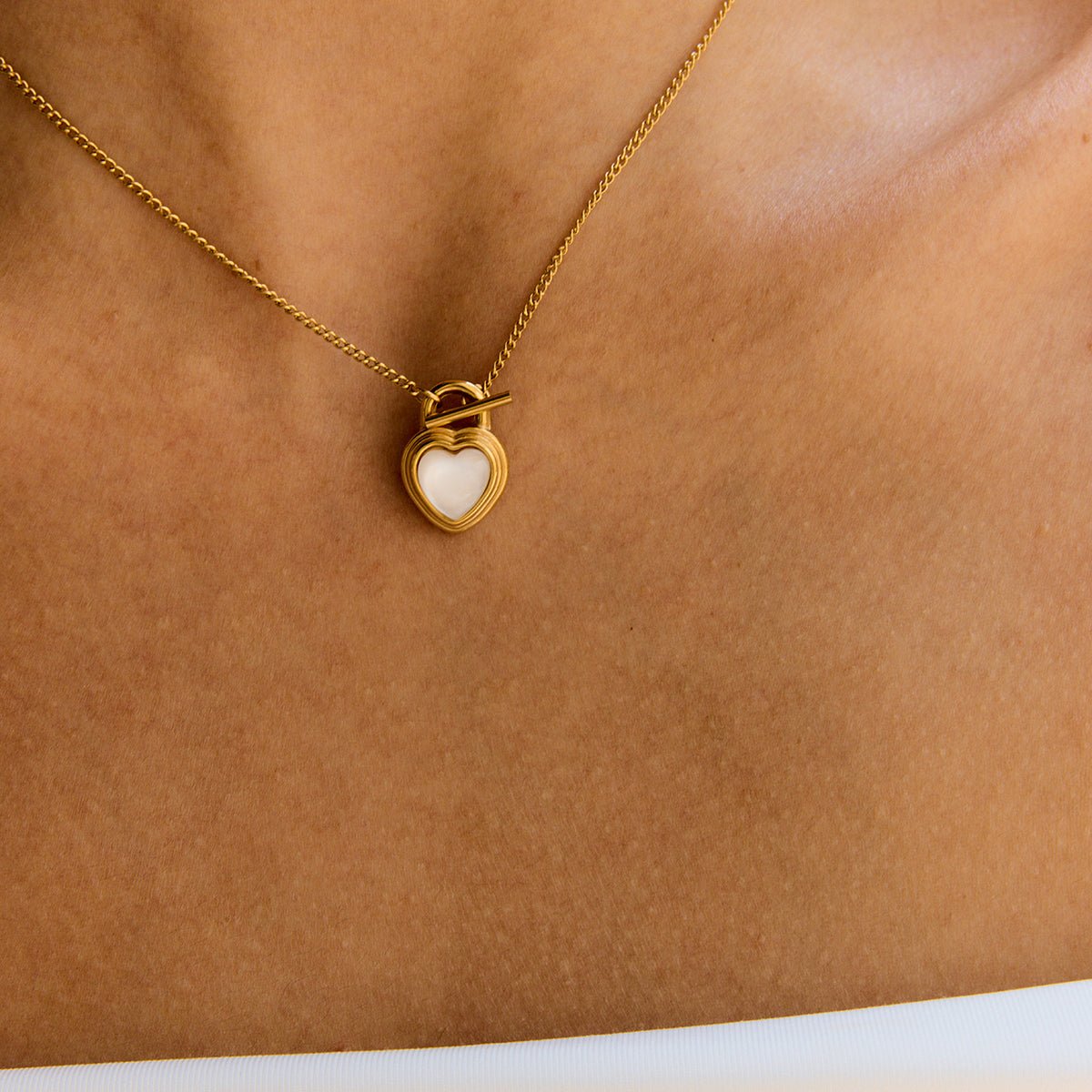 Gold necklace with a heart-shaped pendant on a person's neck