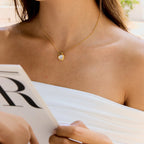 Woman wearing a gold necklace with a heart pendant, holding a magazine.