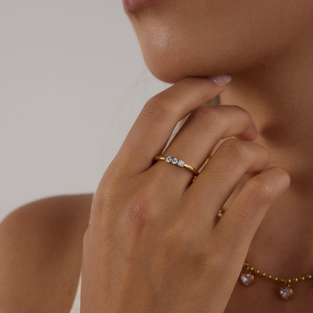 Close-up of a hand wearing a gold ring with small diamonds, against a neutral background.