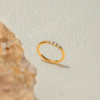 Gold ring with small diamonds on a textured beige background