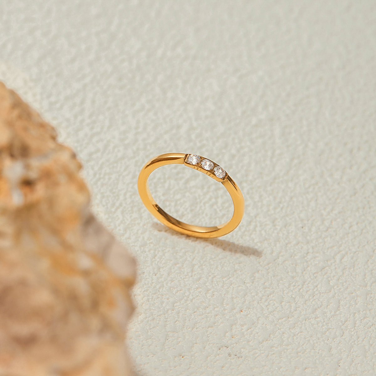Gold ring with small diamonds on a textured beige background