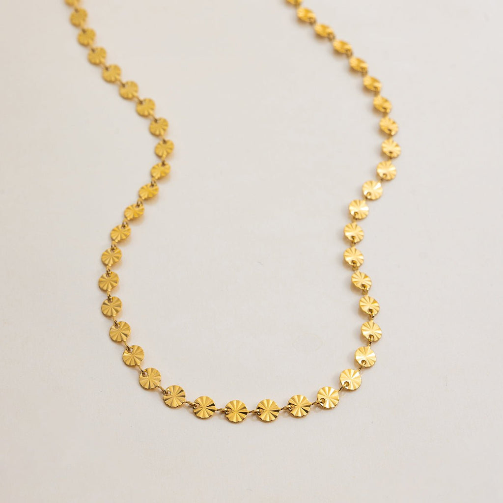 Gold necklace with circular links on a light gray background