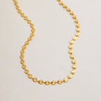 Gold necklace with circular links on a light gray background