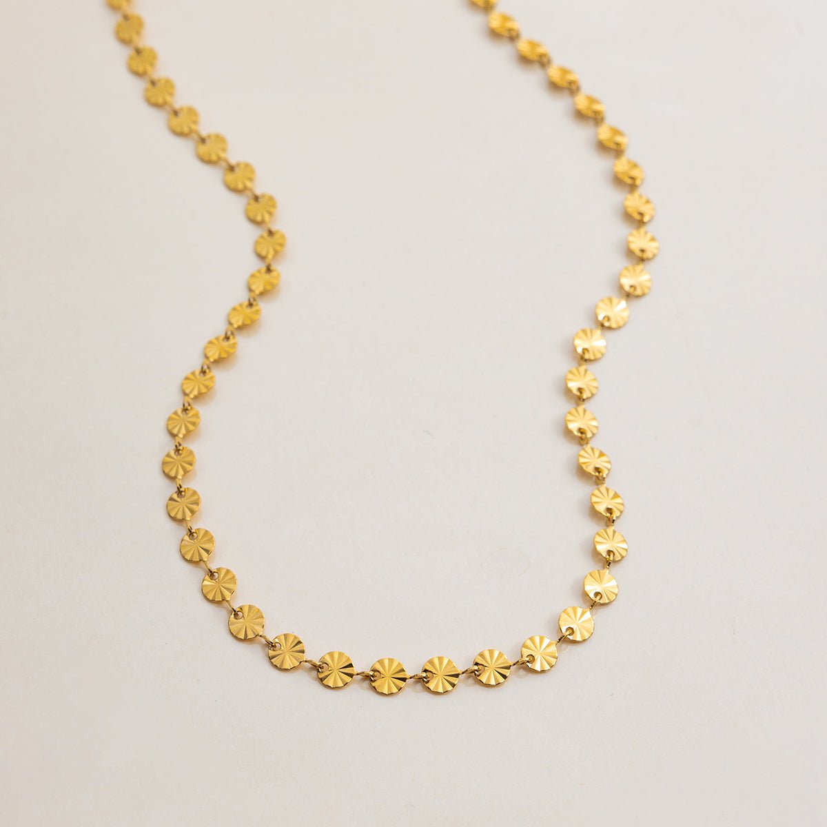 Gold necklace with circular links on a light gray background