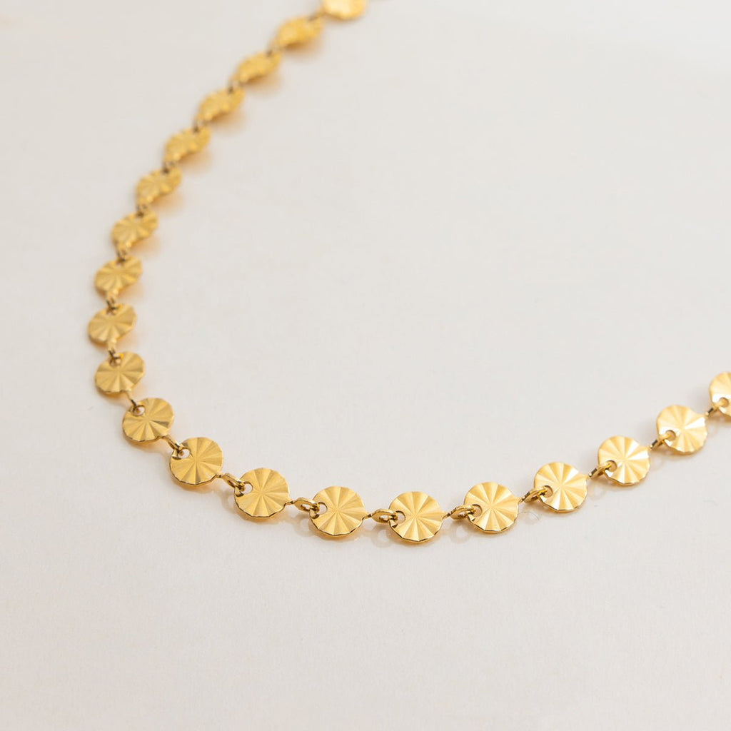 Gold necklace with circular links on a light gray background