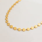 Gold necklace with circular links on a light gray background