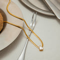Gold necklace with a diamond pendant on a table setting with plates and cutlery.