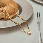 Gold necklace with a heart pendant on a table with bread and cutlery
