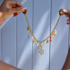 Gold necklace with various charms held by hands against a light blue wooden panel background