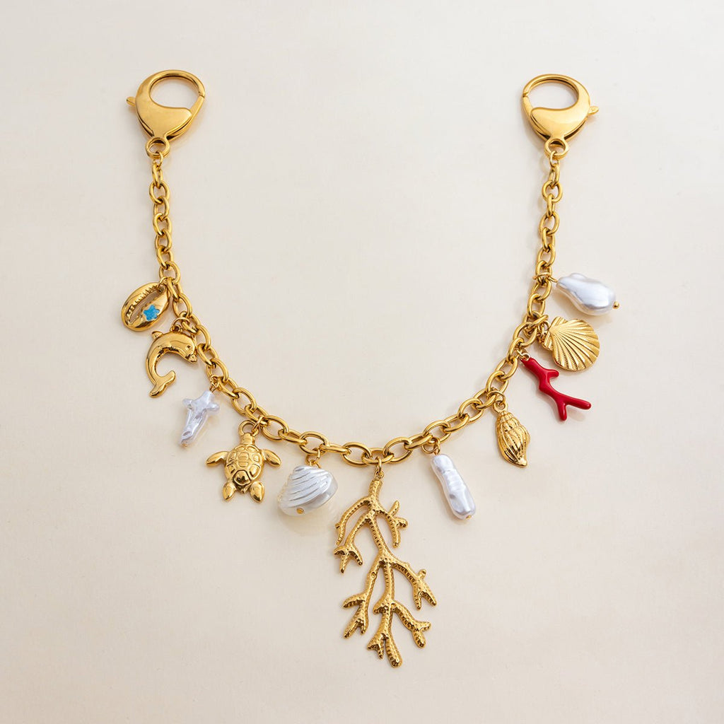 Gold charm bracelet with various sea-themed charms on a beige background