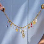 Gold necklace with various charms against a light blue wooden background