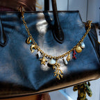 Black handbag with a gold charm necklace draped over it