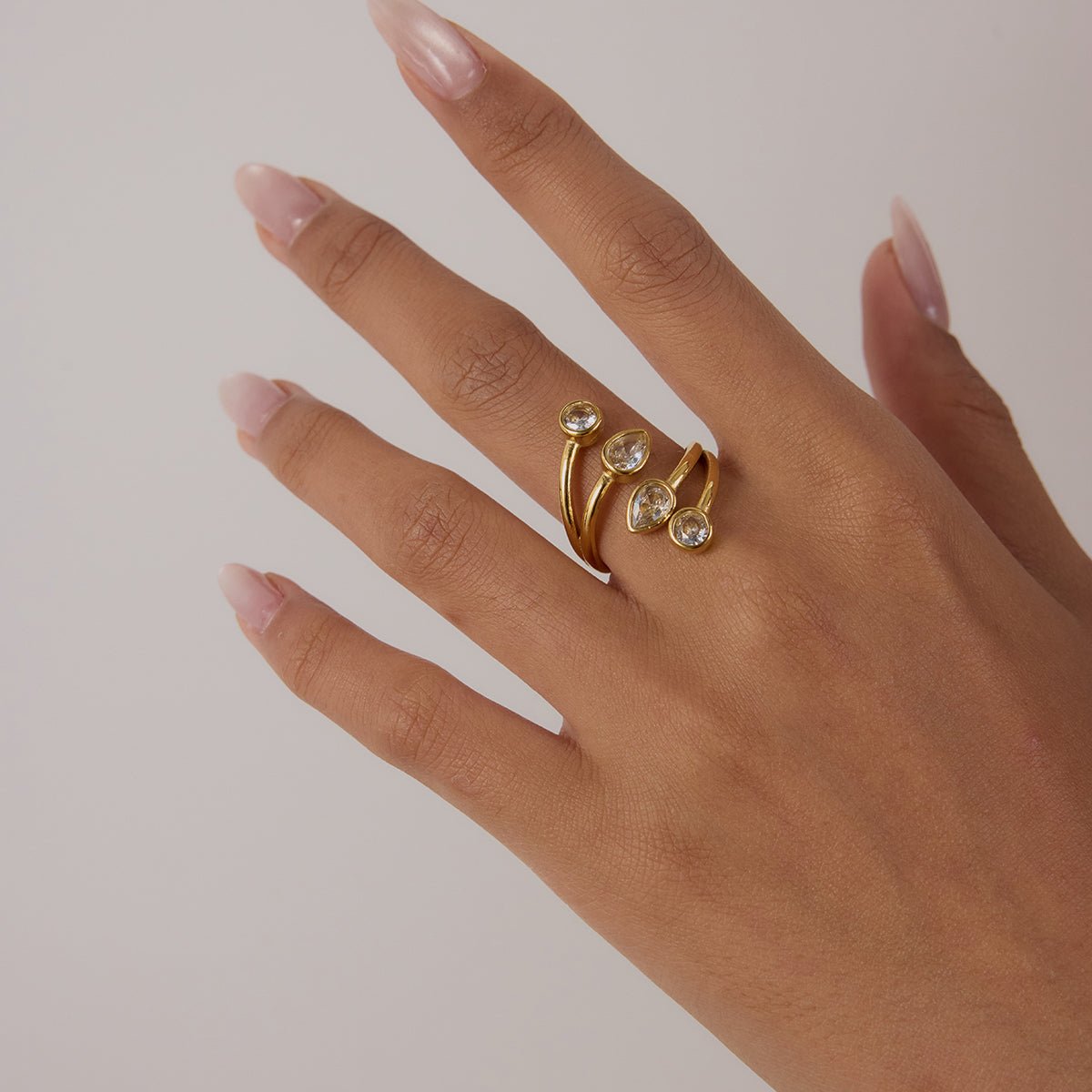 Hand wearing a gold ring with gemstones on a plain background