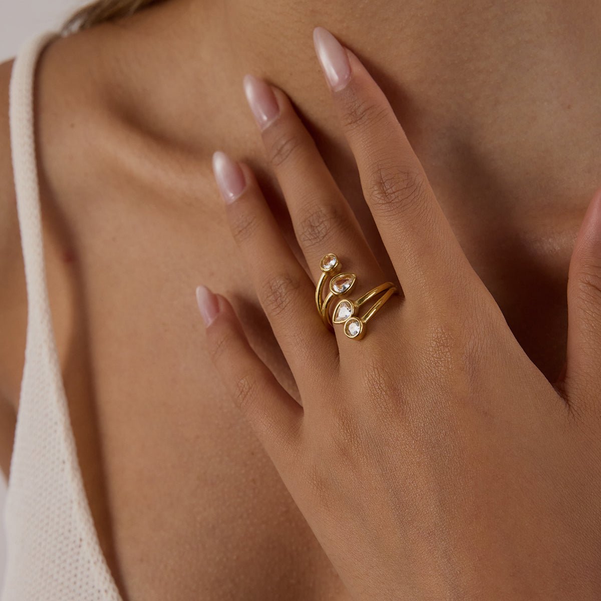 Close-up of a hand wearing a gold ring with pearls on a neutral background