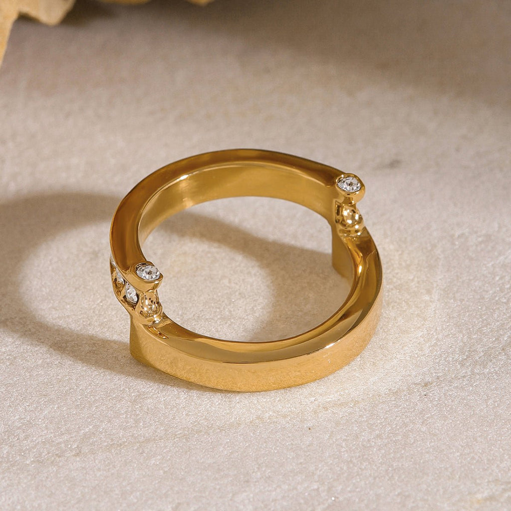 Gold ring with diamond accents on a beige surface