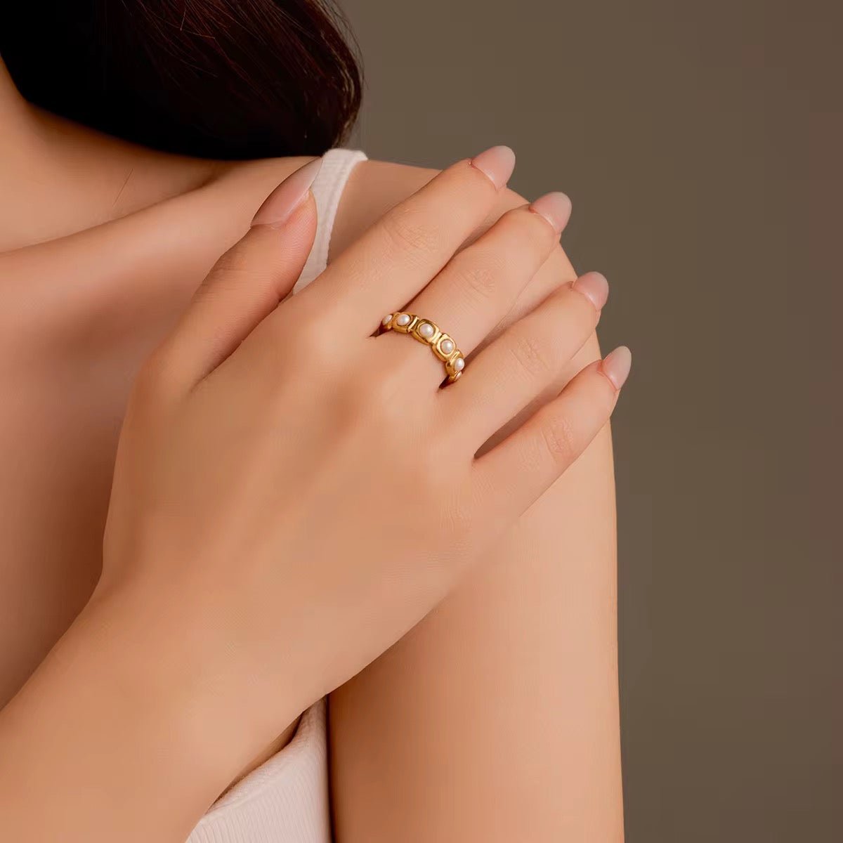 Close-up of a hand wearing a gold ring with gemstones on a neutral background