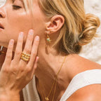 Close-up of a woman wearing gold jewelry including earrings, rings, and a necklace.