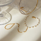 Gold and pearl necklace on a beige surface with a glass object in the background